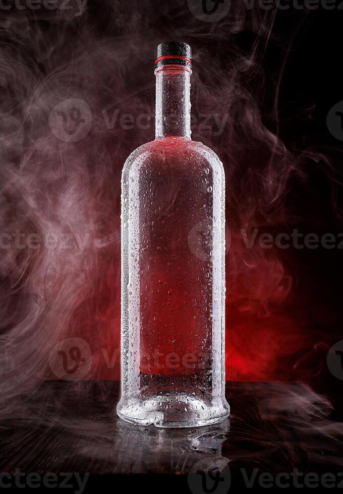 A wet bottle on a beautifully illuminated background. Smoke around a glass bottle. photo