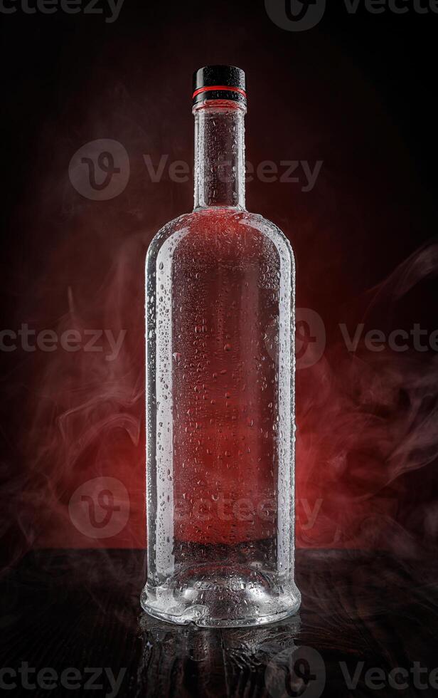 A wet bottle on a beautifully illuminated background. Smoke around a glass bottle. photo