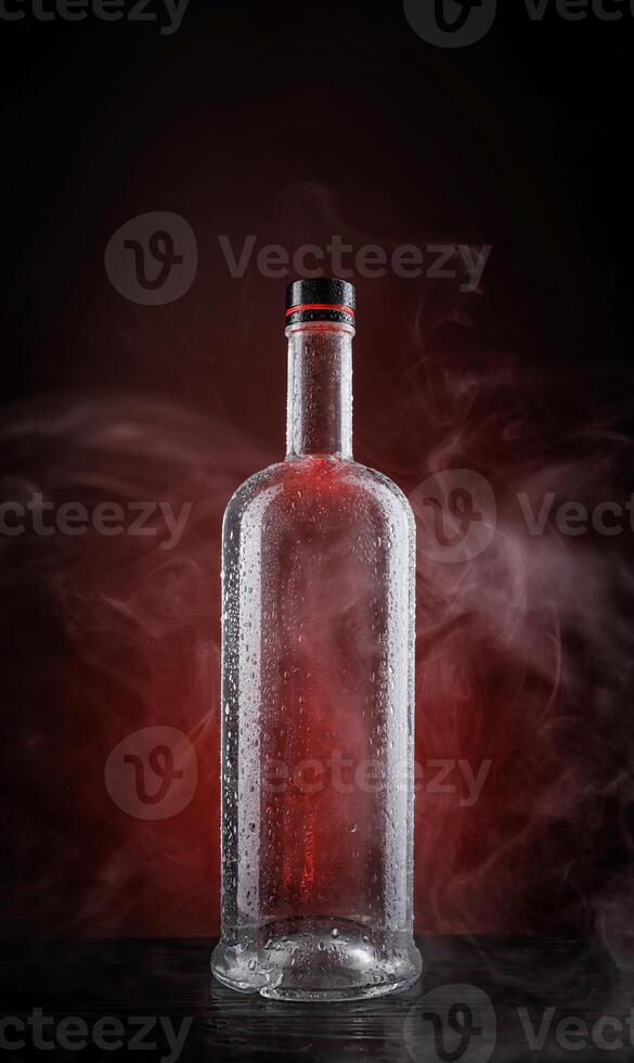 A wet bottle on a beautifully illuminated background. Smoke around a glass bottle. photo