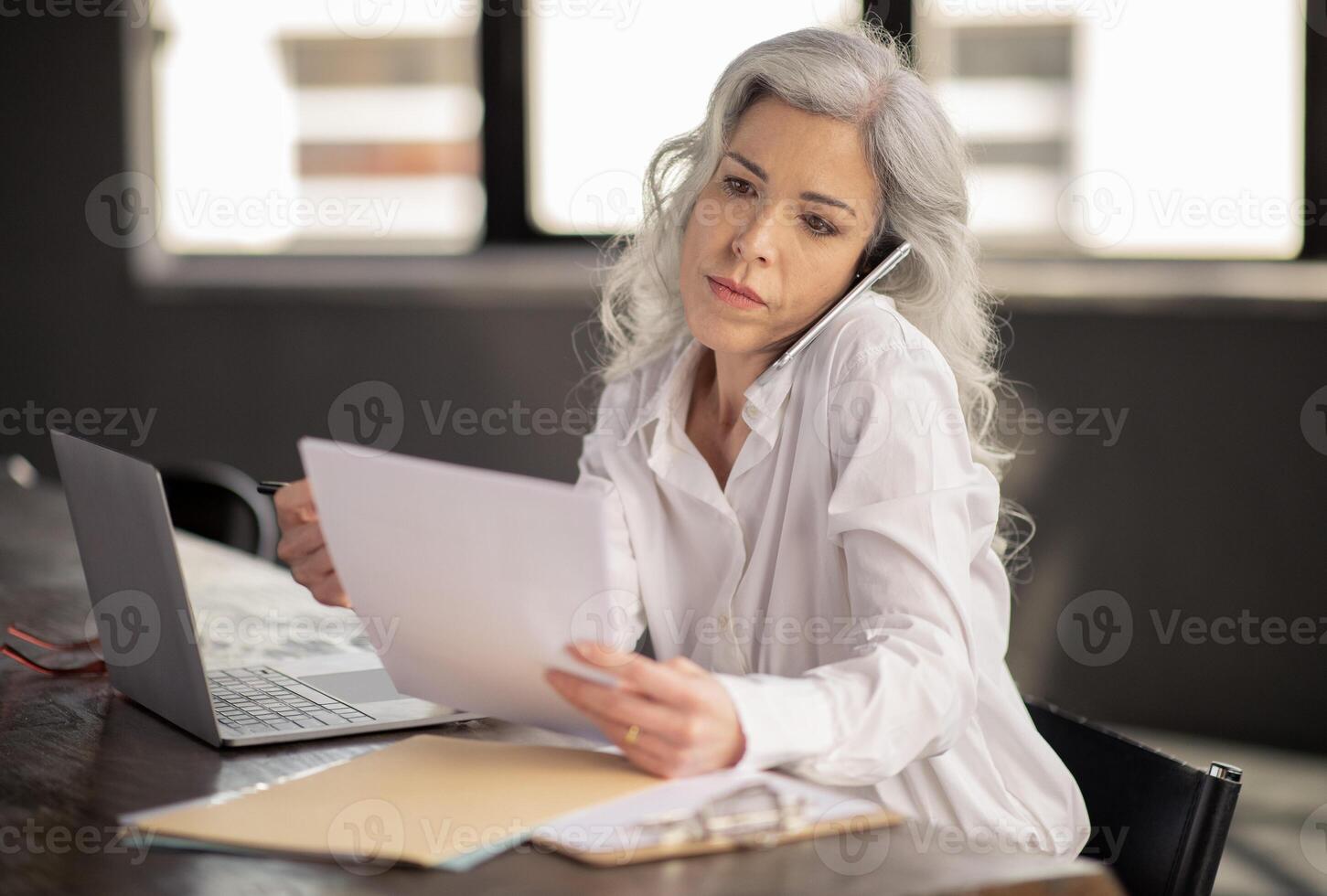 Employment And Communication Issue. Serious HR Manager Talking On Cellphone Employing New Business Professionals Sitting At Workplace In Modern Office, Reading Paper Resumes And CVs At Laptop photo