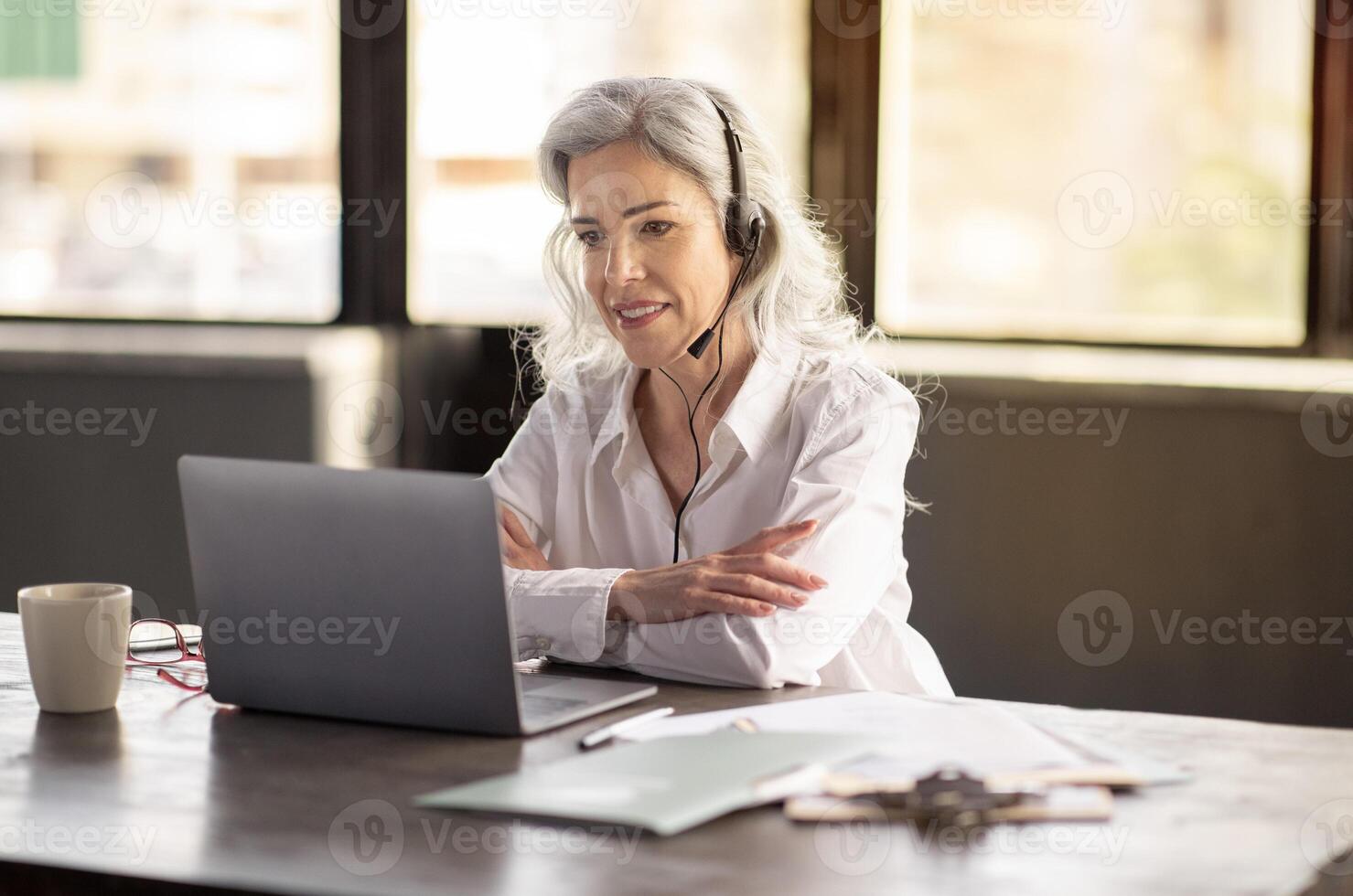 Virtual Business Connection. Professional Woman Engaged In Call Via Laptop, Wearing Headset In Office Interior. Shot Of Customer Support Manager Lady Assisting Clients Remotely photo