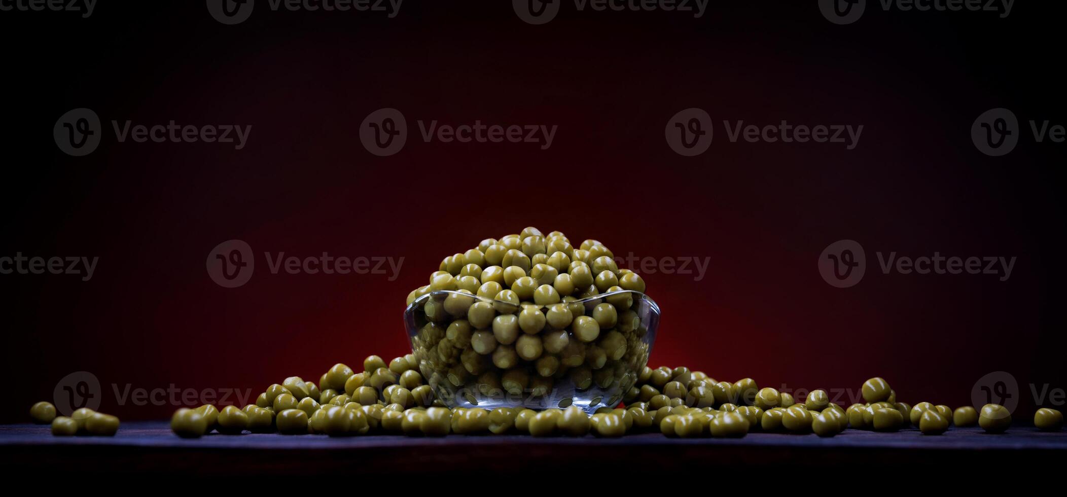 Canned green peas in a glass cup and scattered around it. Beautifully illuminated background. photo