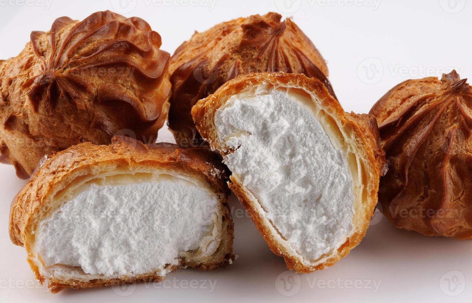 Cut in half and whole porophytroles with white cream on a white background. Eclair with cream. photo