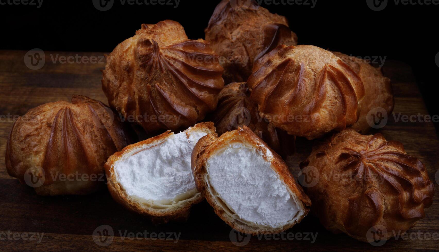 Profiteroles with white custard on a wooden board. Mini eclairs with white cream. photo