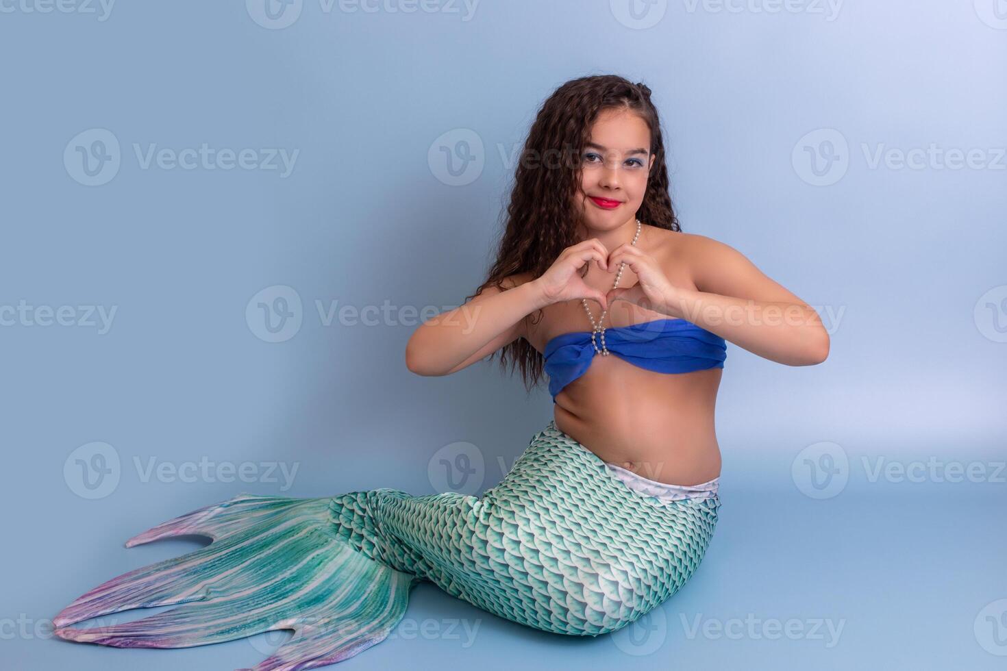 A pretty child girl in a mermaid costume, sitting on a blue background photo