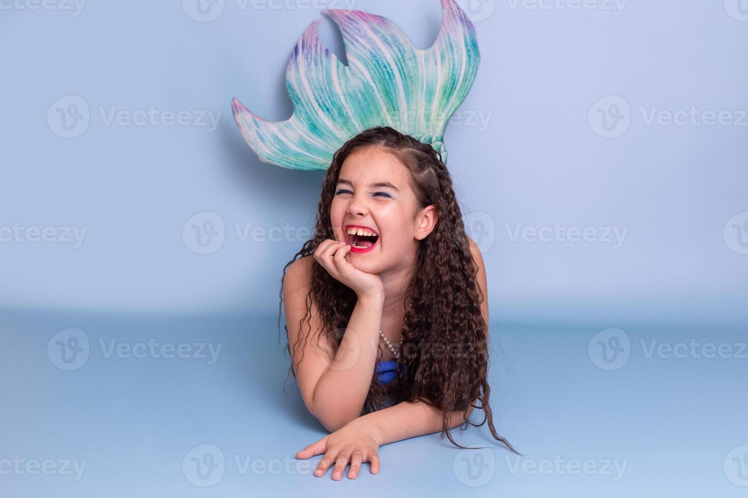 A very happy child girl in a mermaid costume lie isolated on light-blue background photo