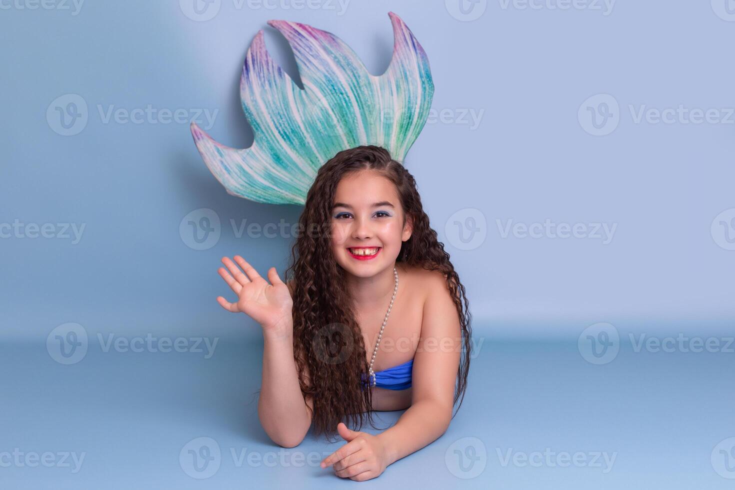 Cute girl in a mermaid costume, friendly, lies on a blue background photo