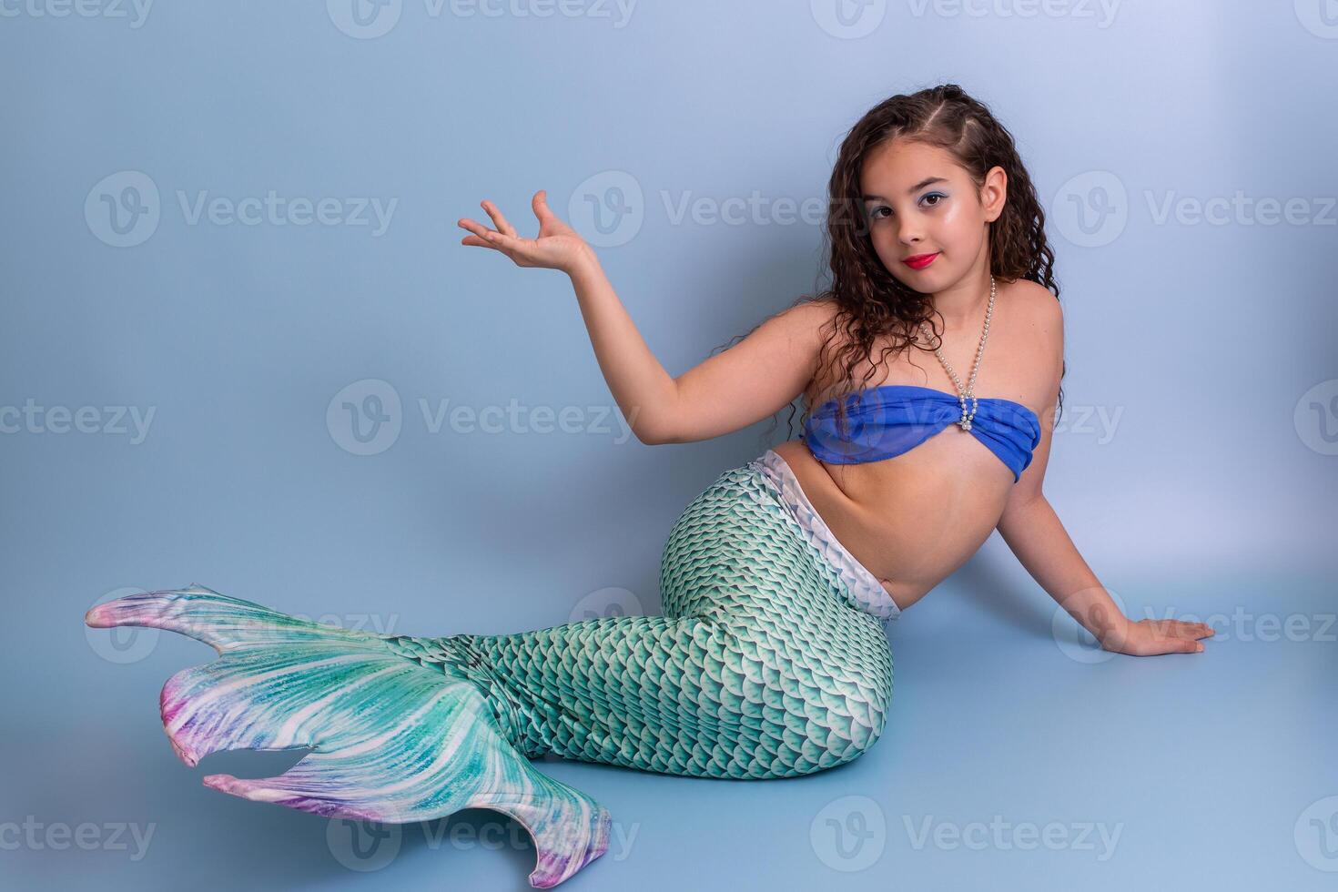 A beautiful elegant girl in a mermaid costume lies on a blue background with her palm raised up. photo