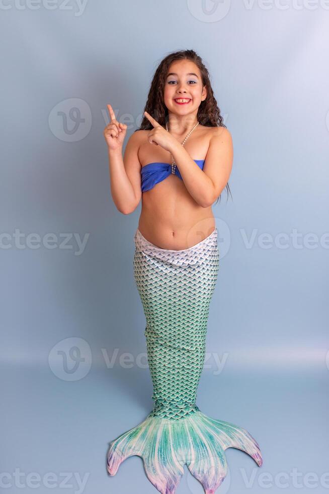A beautiful child girl in a mermaid costume stand on a blue background photo