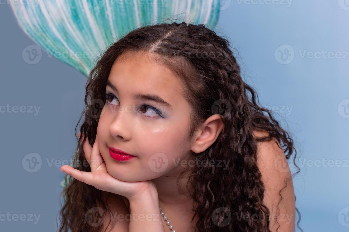 Close up of cute girl in a mermaid costume lie on light-blue background photo