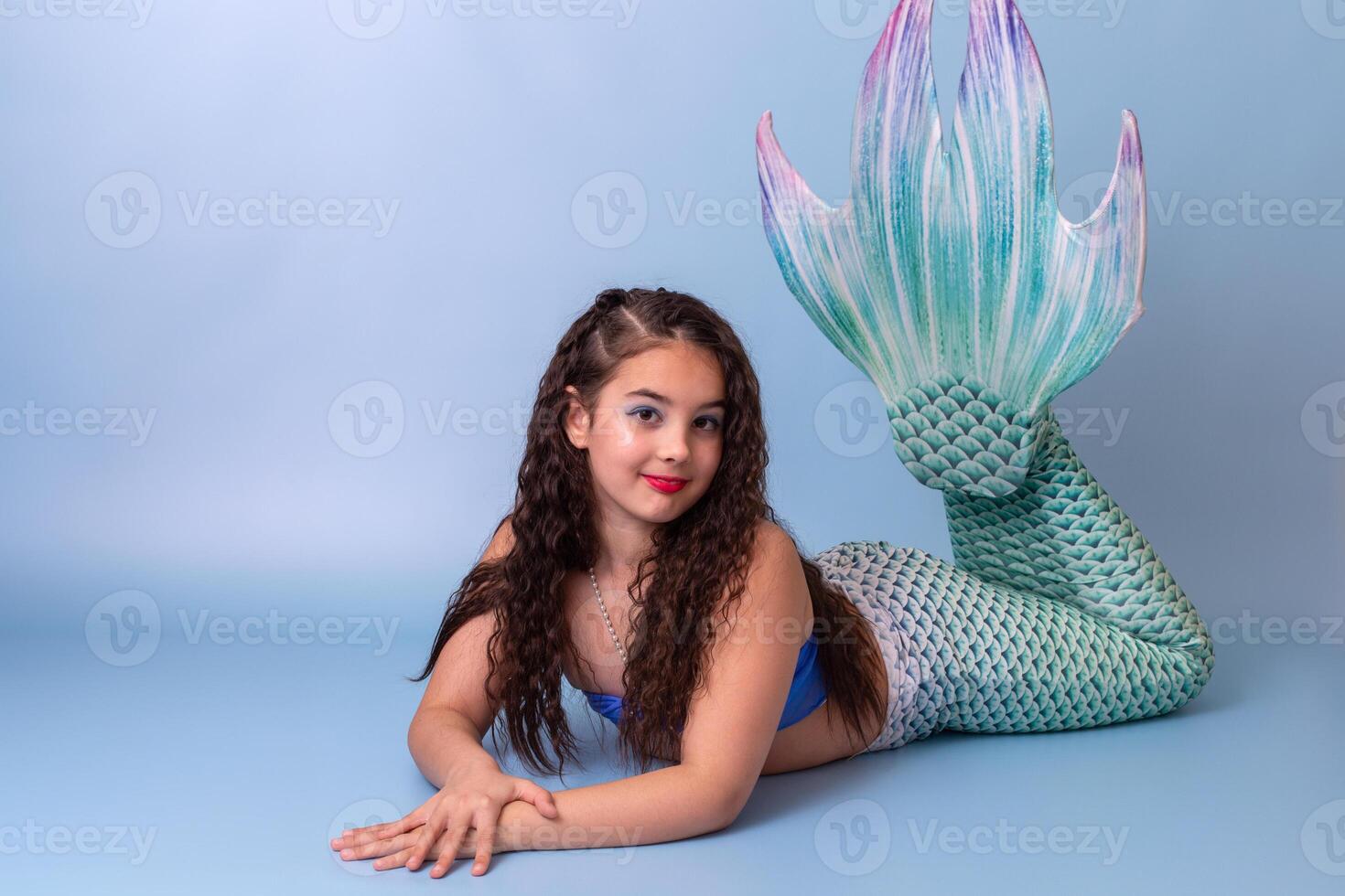 A pretty child girl in a mermaid costume lie isolated on light-blue background photo
