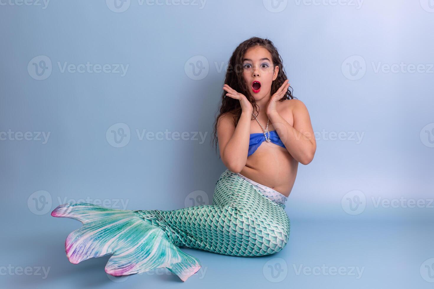 Shocked girl in mermaid costume sitting on blue background photo