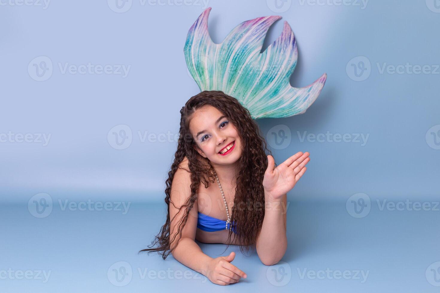 Beautiful smiling girl in a mermaid costume, friendly, lies on a blue background . Copy space photo