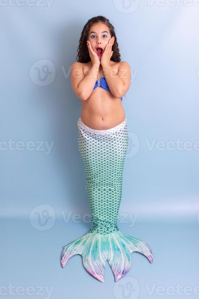 Beautiful surprised girl in mermaid costume stand on blue background photo