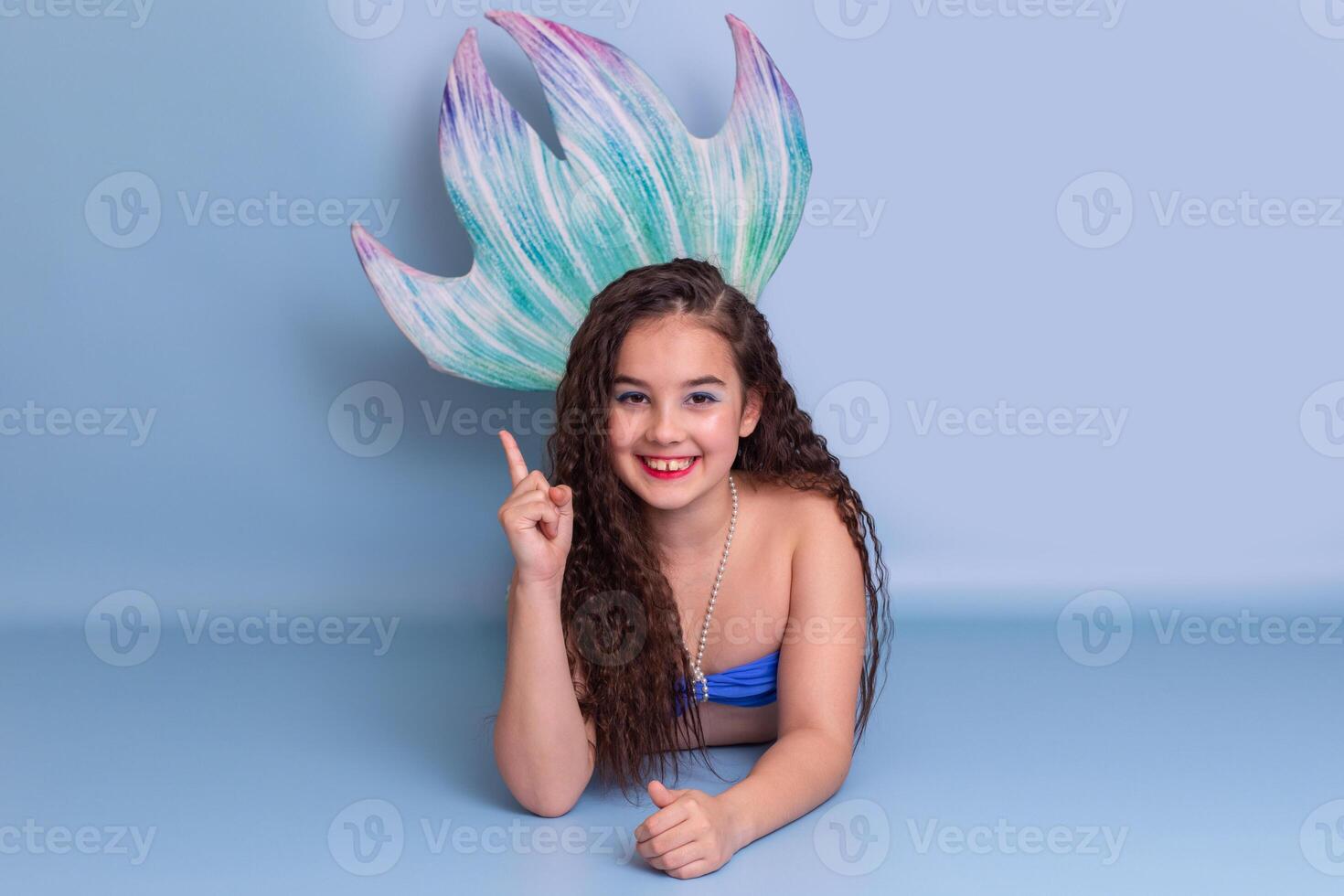 A cute child girl in a mermaid costume lie on a blue background photo