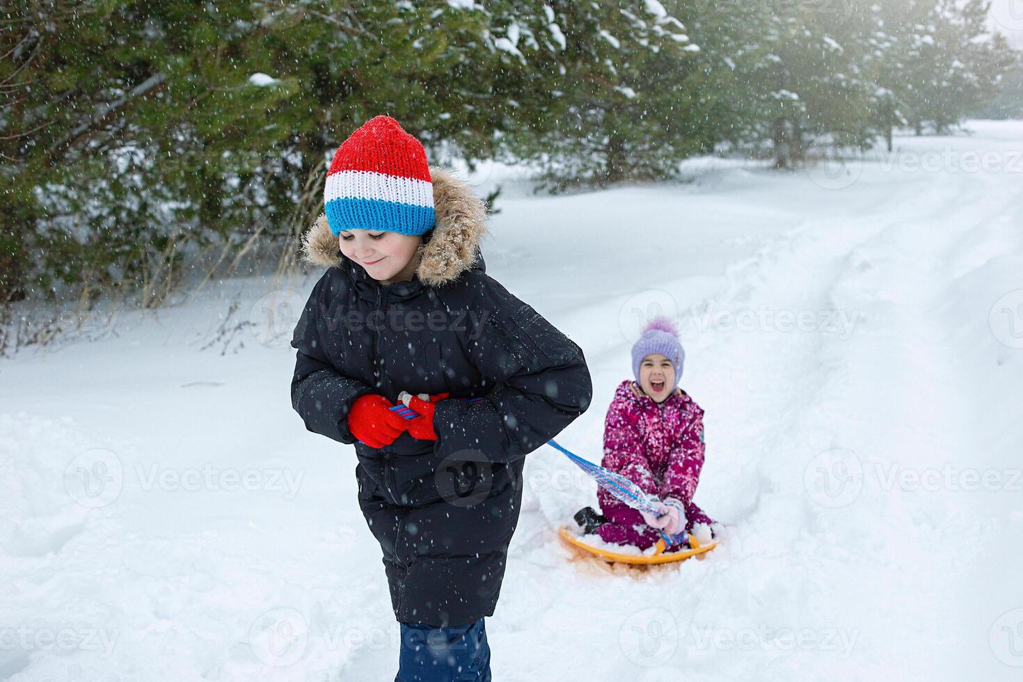 A teenage boy rolls a little girl in the snow on a plastic ice rink. photo