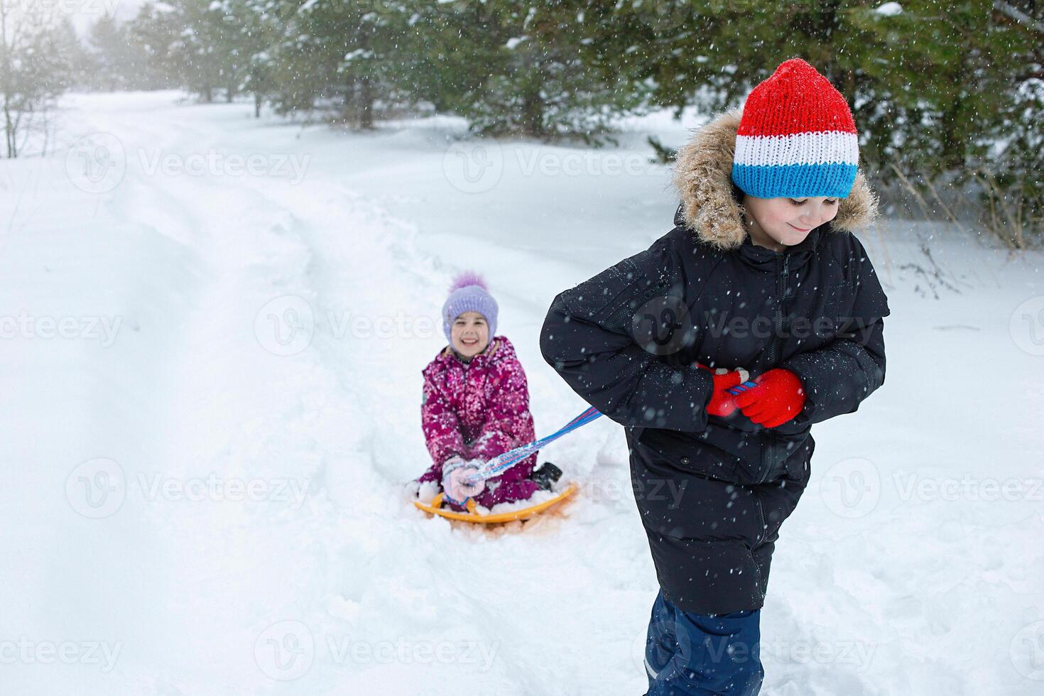 A teenage boy rolls a little girl in the snow on a plastic ice rink. photo