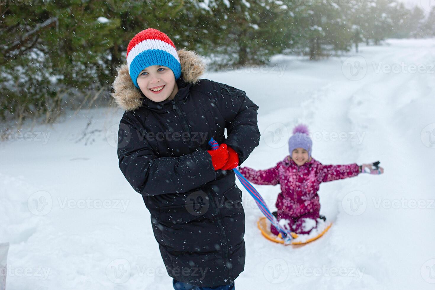 A happy teenage boy rolls a little girl in the snow on a plastic ice rink. photo
