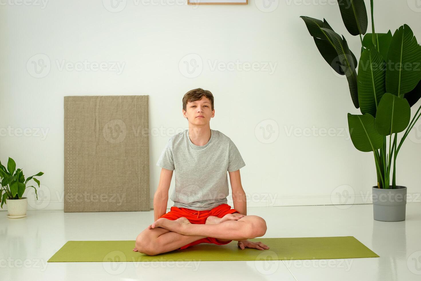 A teen boys sit in the lotus position, in a bright room photo