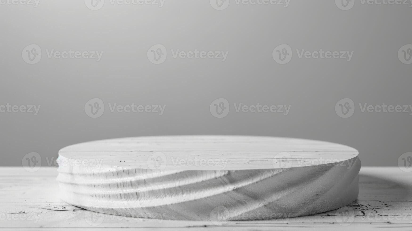 A round wooden platform stands on a white marble surface under soft lighting. The background is plain and gray, creating a minimalist look. photo