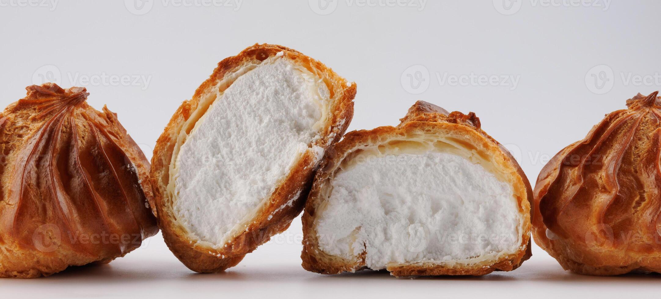 Cut in half and whole porophytroles with white cream on a white background. Eclair with cream. photo