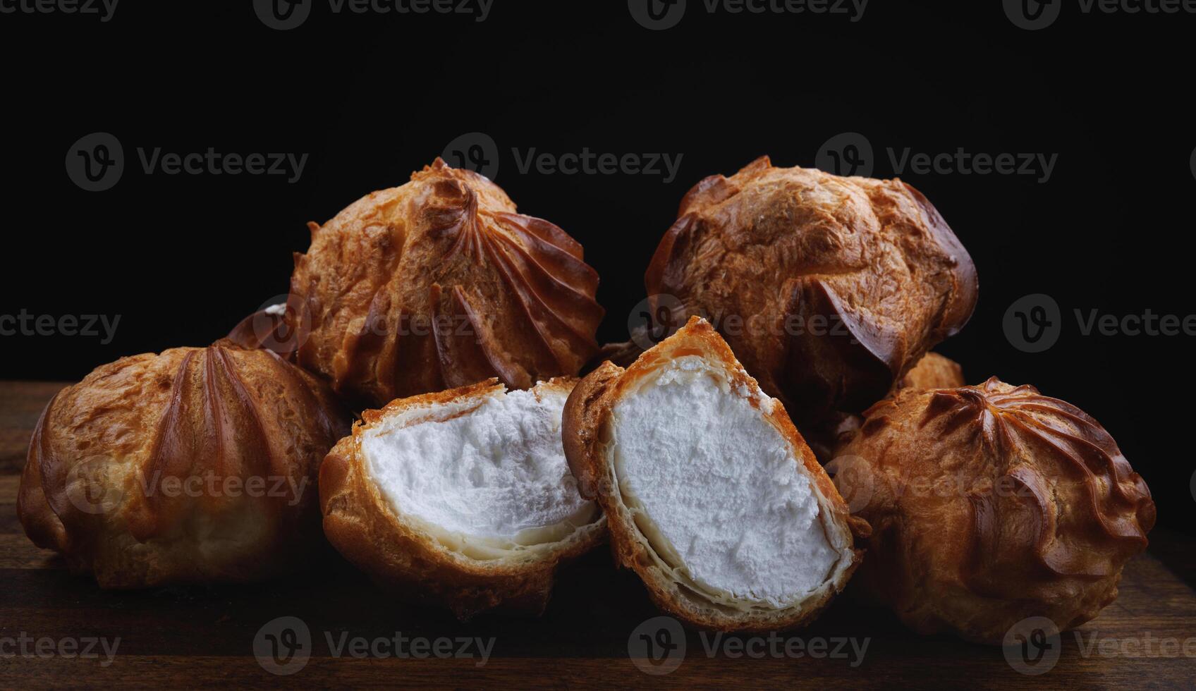 Profiteroles with white custard on a wooden board. Mini eclairs with white cream. photo