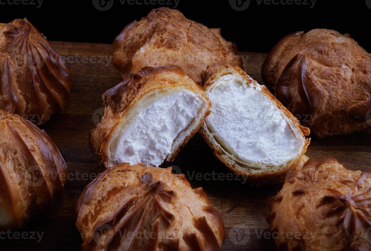 Profiteroles with white custard on a wooden board. Mini eclairs with white cream. photo