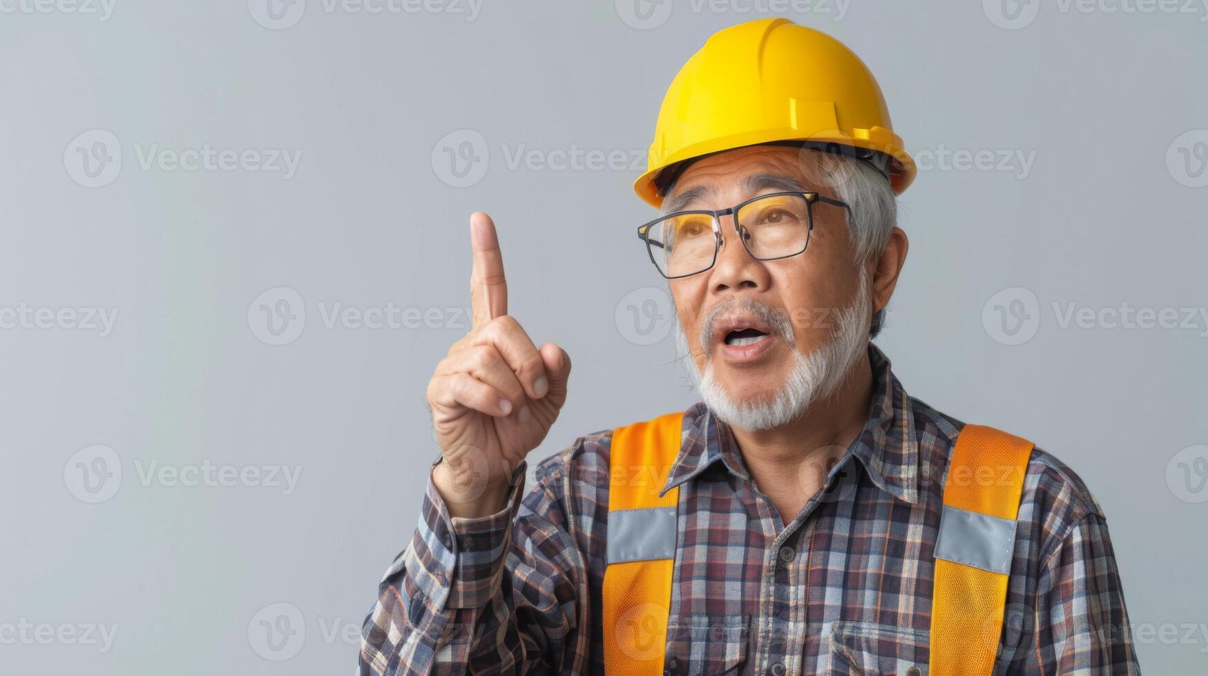 An elderly asian man, wearing a hard hat, pointing at something off-screen with a serious expression. photo