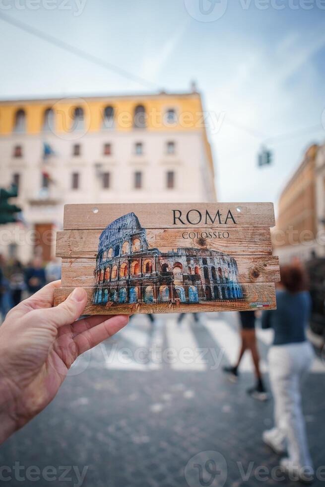 Hand holding Colosseum postcard in Rome, Italy. Seamless transition from postcard to real buildings creating intriguing visual effect. Urban setting with European architectural style. photo