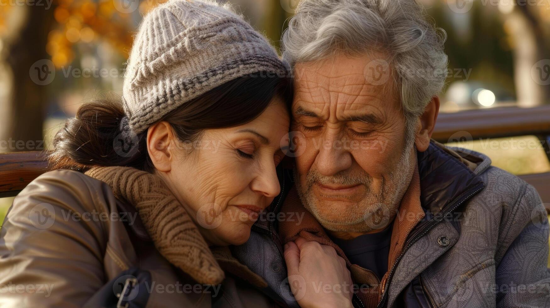 A husband and wife sitting on a bench comforting each other while their aging parent rests nearby photo