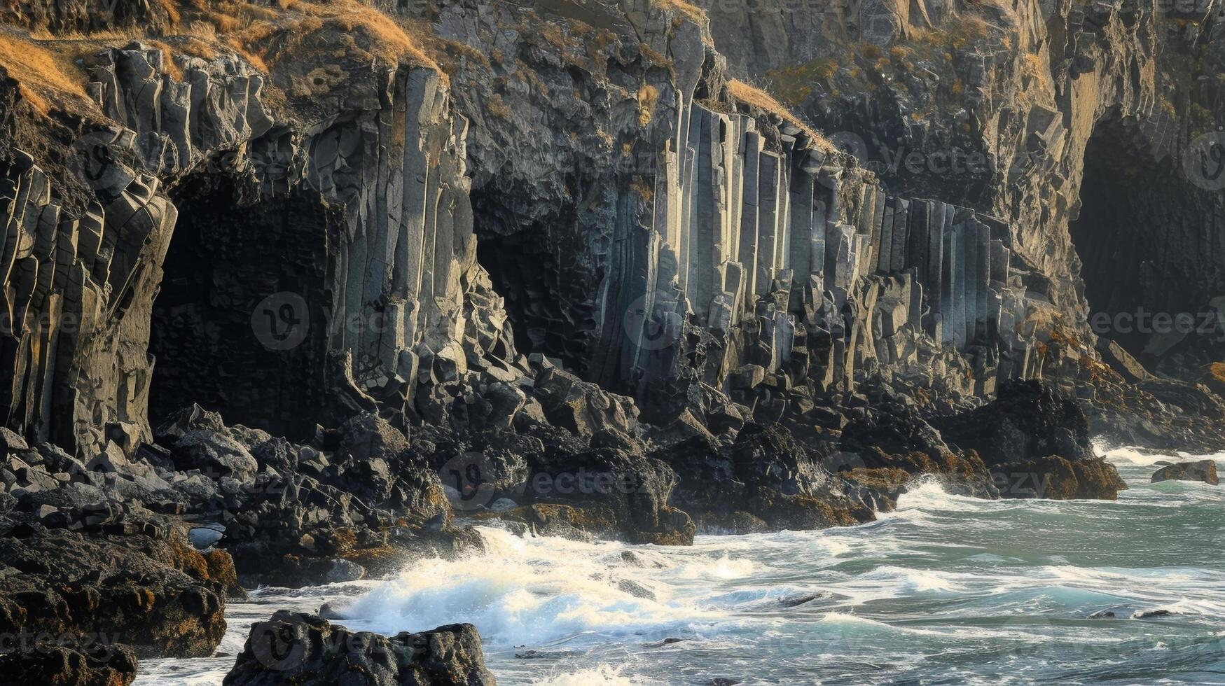 The rugged coastline dotted with tall angular basalt columns formed by the constant beating of the waves photo