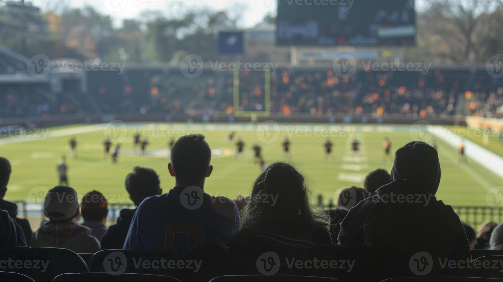 In the foreground a blurry scene of students gathering in the stands with the distant sound of cheers and the faint silhouette of players on the field encapsulating the sense of photo