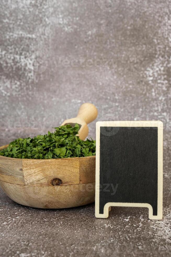 Dry parsley spice in wooden bowl with empty blackboard mock up template. Homegrown herbs and spices for cooking. Fresh dried aromatic natural food ingredients. Copy space photo