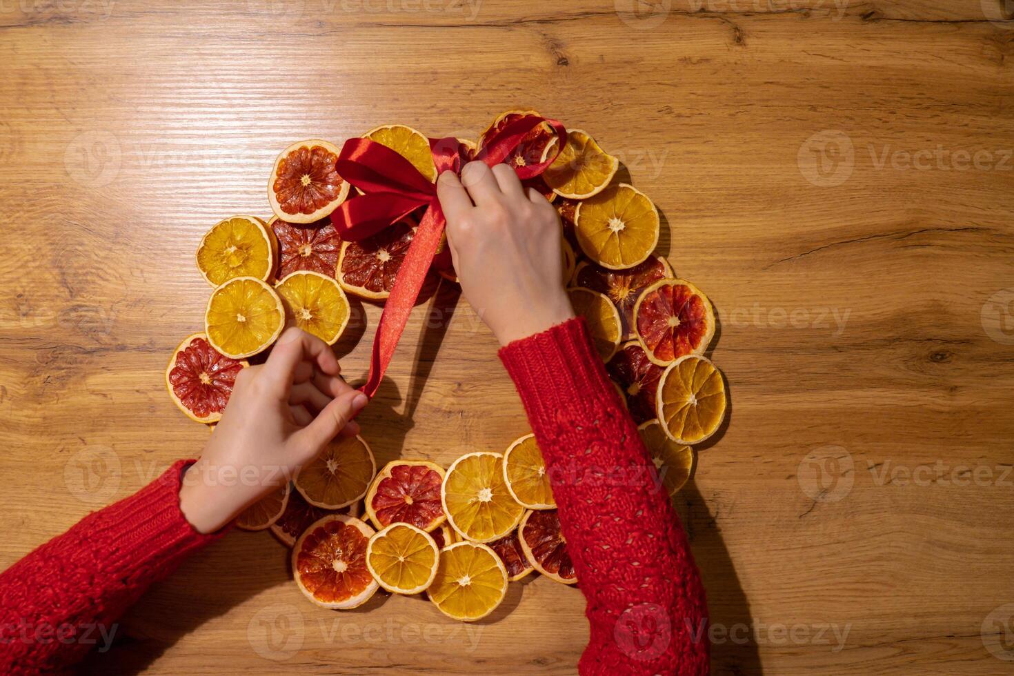 Handmade tying ribbon Christmas wreath from dried orange grapefruit slices. Festive holiday preparation craft master class of creative making decor. Hands-on activities sustainable responsible holiday gift workshop creation. Top view, flat lay photo
