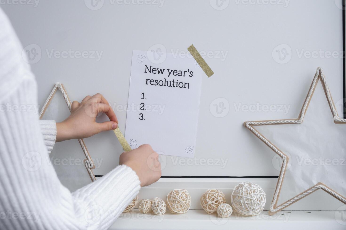Unrecognizable woman creating vision board. NEW YEAR'S RESOLUTION checklist text on paper note stick on while wall with cozy minimalistic handmade Christmas decor. New year aims resolutions. Low key festive Planning and setting goals concept photo