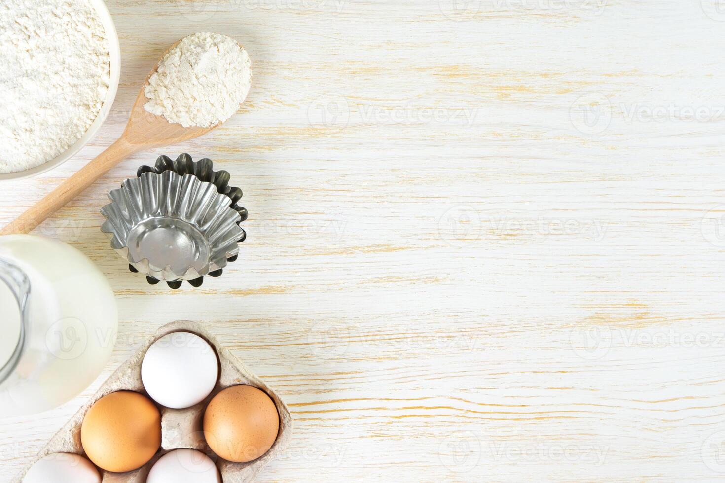 Baking ingredients flour, eggs, milk, bakeware on white wooden background with copy space photo