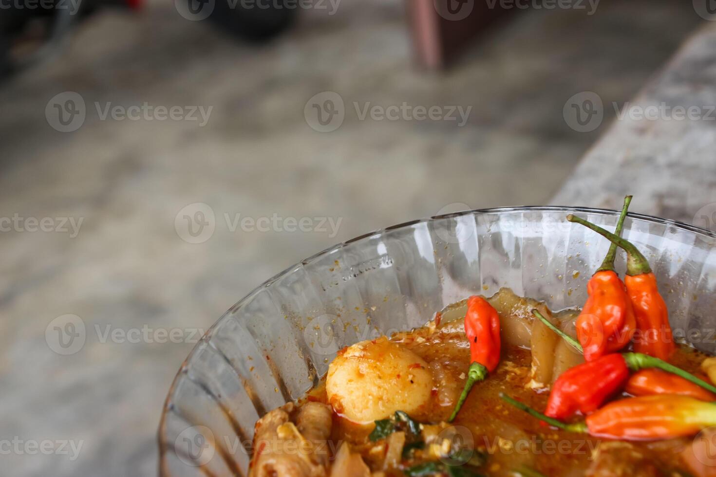 Seblak is a Indonesian dish with a savory and spicy taste. Made from wet crackers cooked with vegetables, sausage, eggs, chicken feet, seafood and processed beef. a bowl of seblak on a wooden table. photo