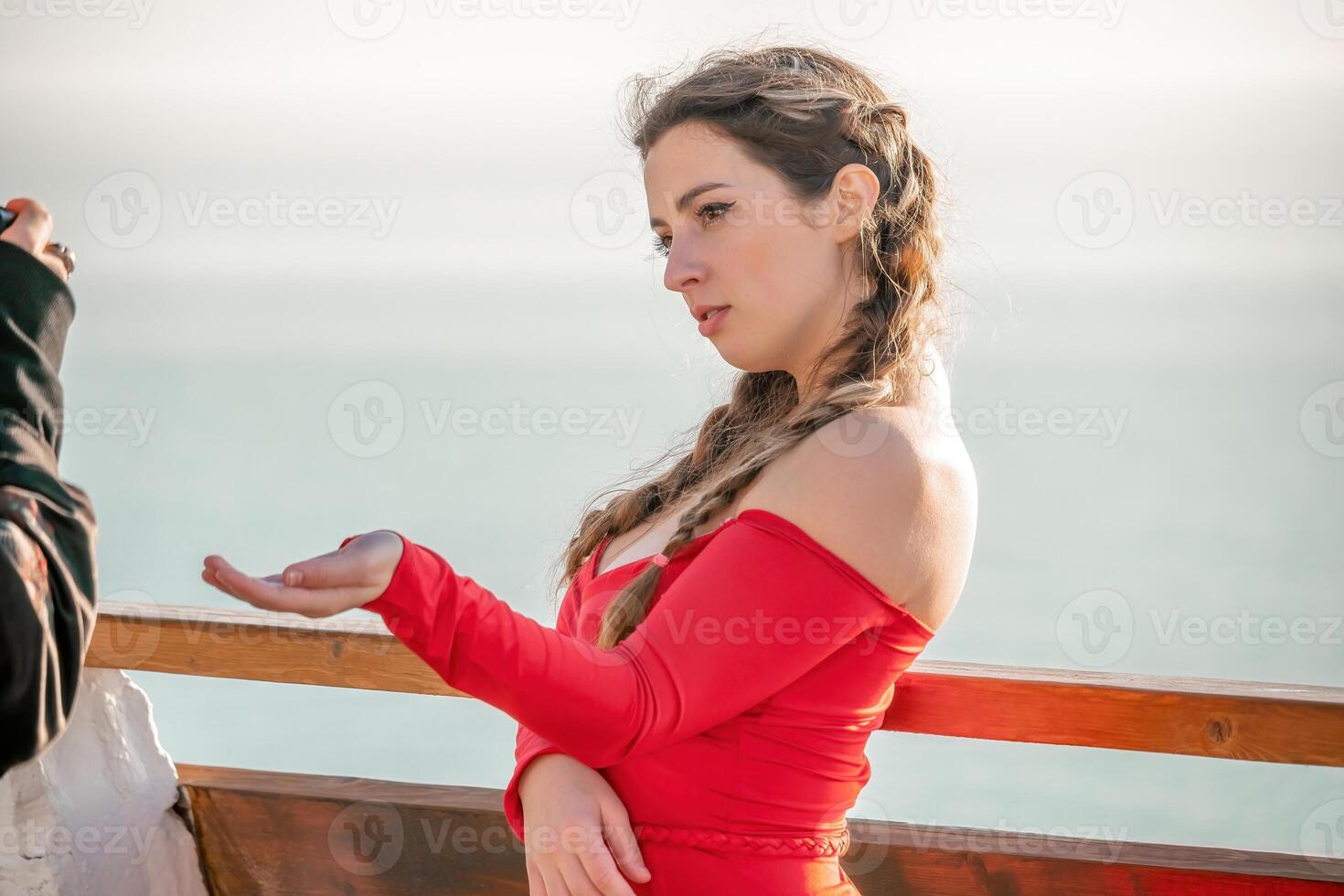 Closeup portrait of sensual young brunette woman in red dress, happily dancing outdoors isolated on blurry sea background with natural bokeh in soft warm sunset backlight. Selective focus. photo