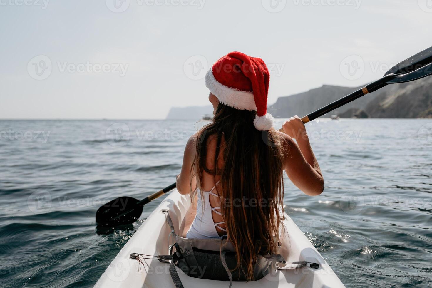 Woman in kayak back view. Happy young woman in Santa hat floating in kayak on calm sea. Summer holiday vacation and cheerful female people relaxing having fun on the boat. photo