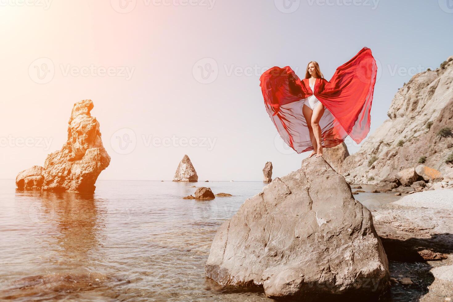 Woman travel sea. Young Happy woman in a long red dress posing on a beach near the sea on background of volcanic rocks, like in Iceland, sharing travel adventure journey photo