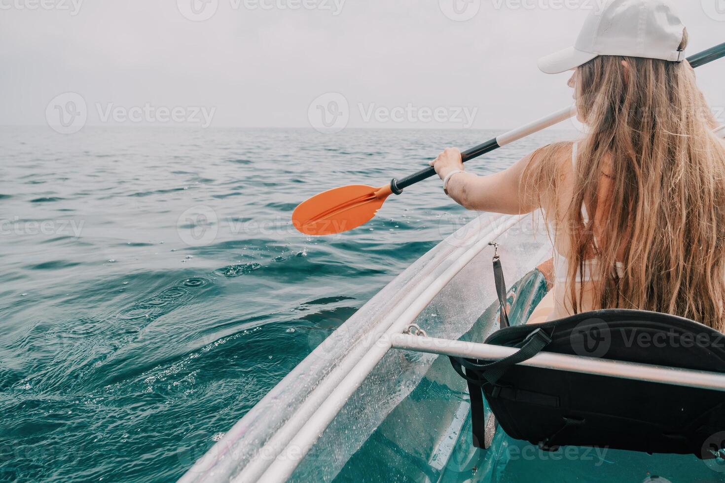 Woman in kayak back view. Happy young woman with long hair floating in transparent kayak on the crystal clear sea. Summer holiday vacation and cheerful female people relaxing having fun on the boat photo