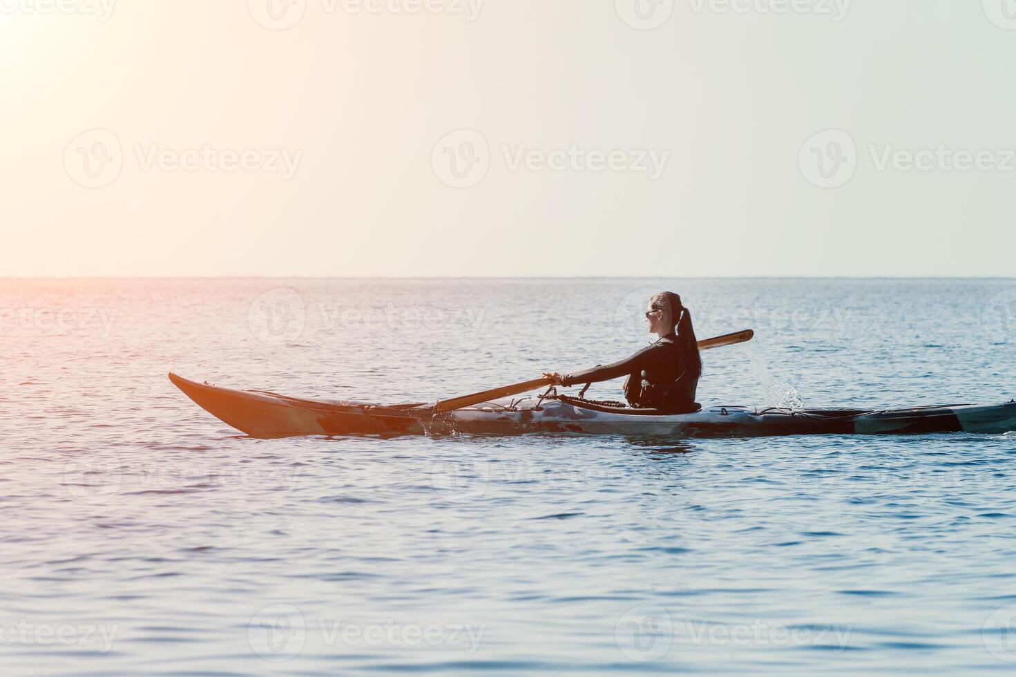 Woman sea kayak. Happy smiling woman in kayak on ocean, paddling with wooden oar. Calm sea water and horizon in background. Active lifestyle at sea. Summer vacation. photo