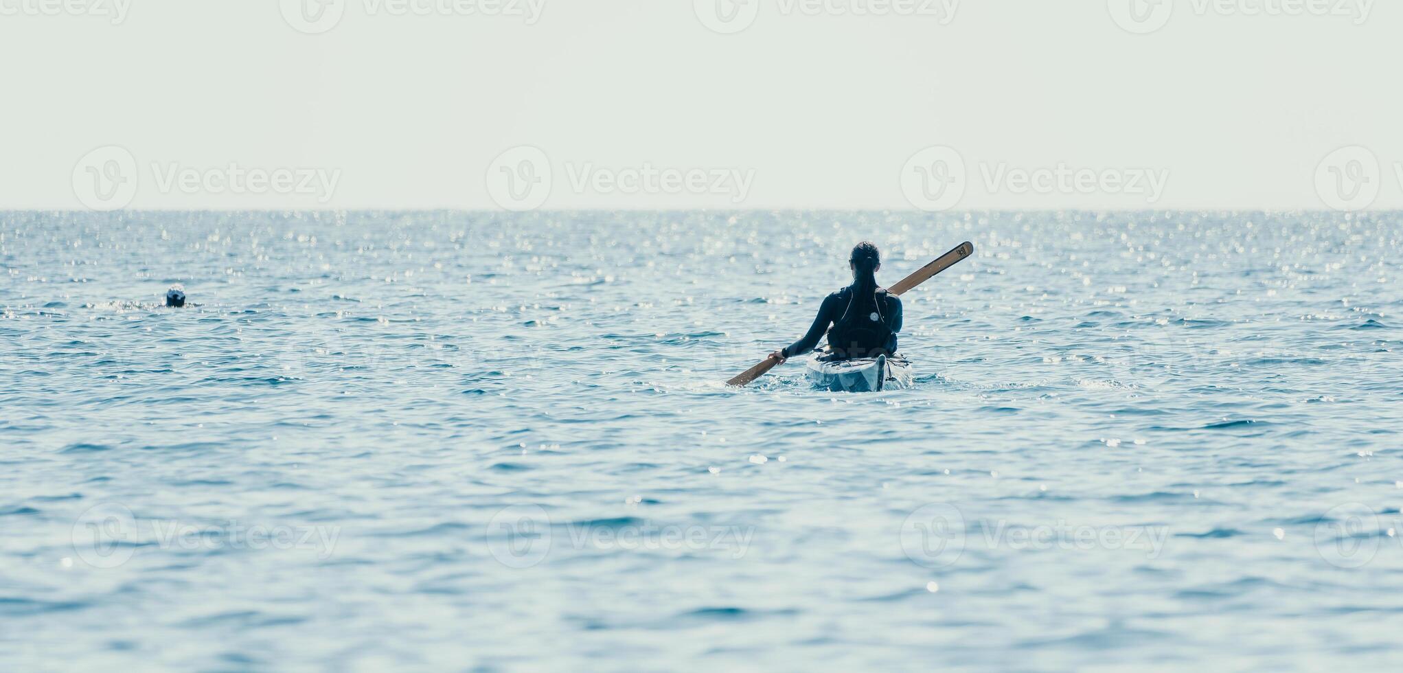 Woman sea kayak. Happy smiling woman in kayak on ocean, paddling with wooden oar. Calm sea water and horizon in background. Active lifestyle at sea. Summer vacation. photo