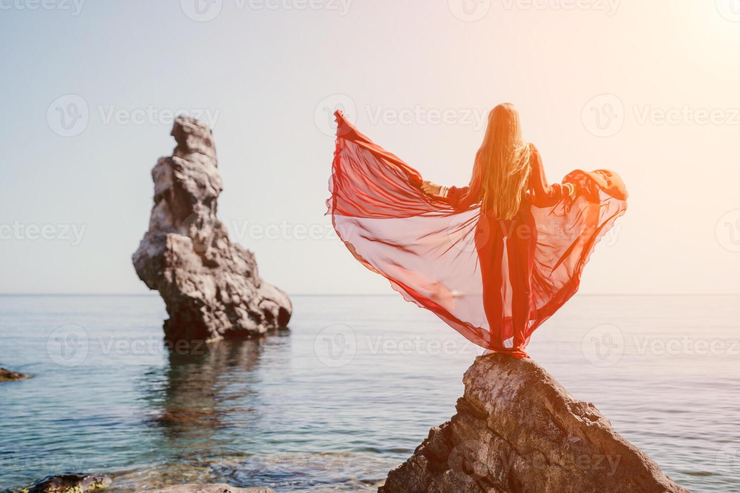 Woman travel sea. Young Happy woman in a long red dress posing on a beach near the sea on background of volcanic rocks, like in Iceland, sharing travel adventure journey photo