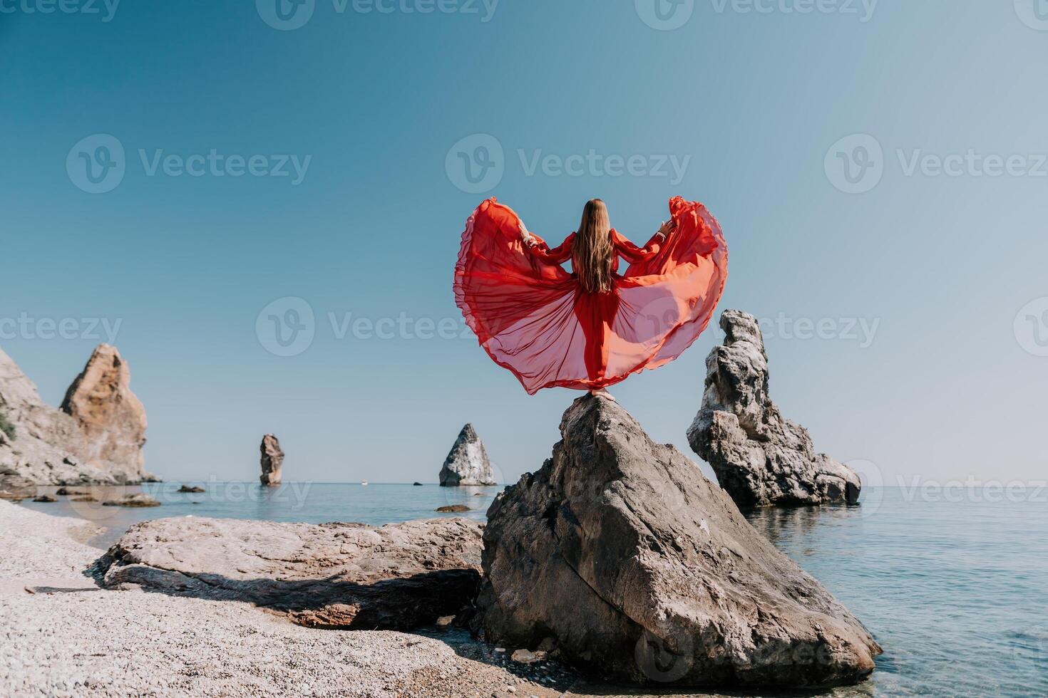 Woman travel sea. Young Happy woman in a long red dress posing on a beach near the sea on background of volcanic rocks, like in Iceland, sharing travel adventure journey photo
