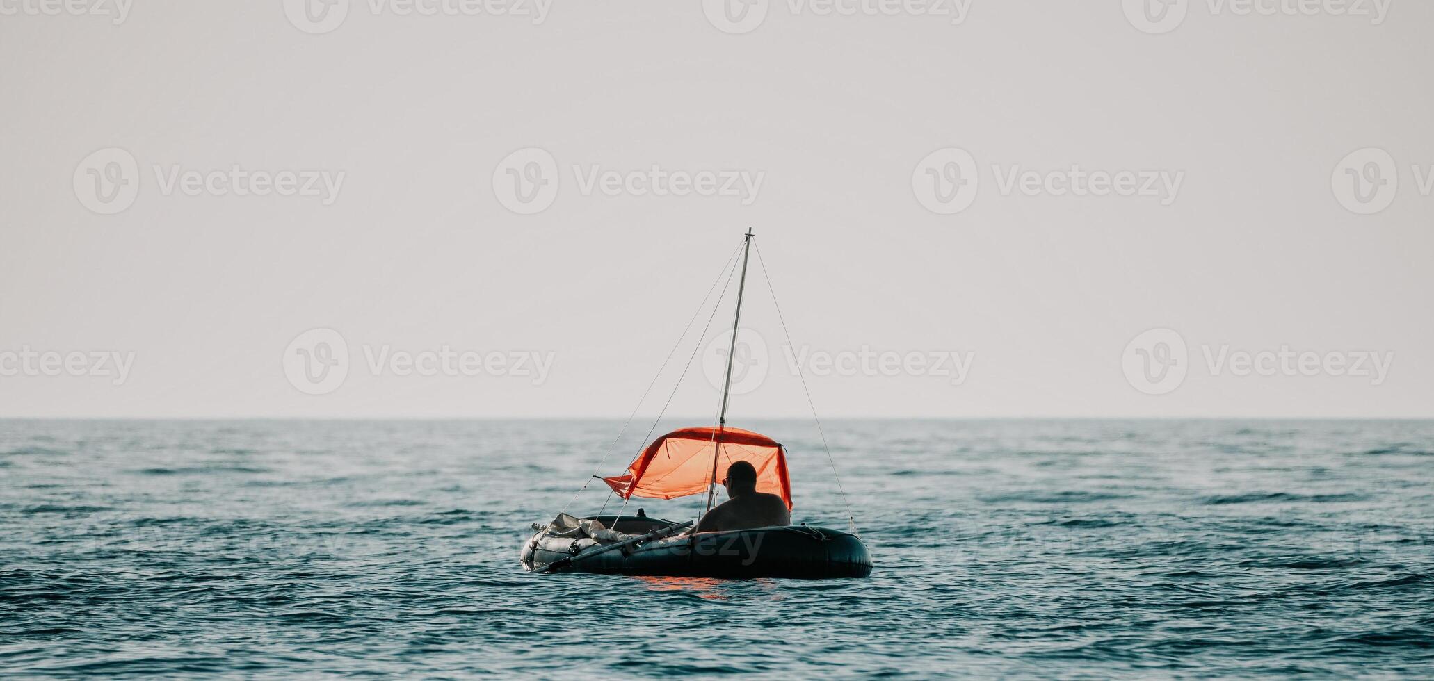 Fisher sea boat. Tourist maneuvering an inflatable boat while fishing in a life jacket, with the beautiful sunset sea in the background. a relaxing fishing trip. photo