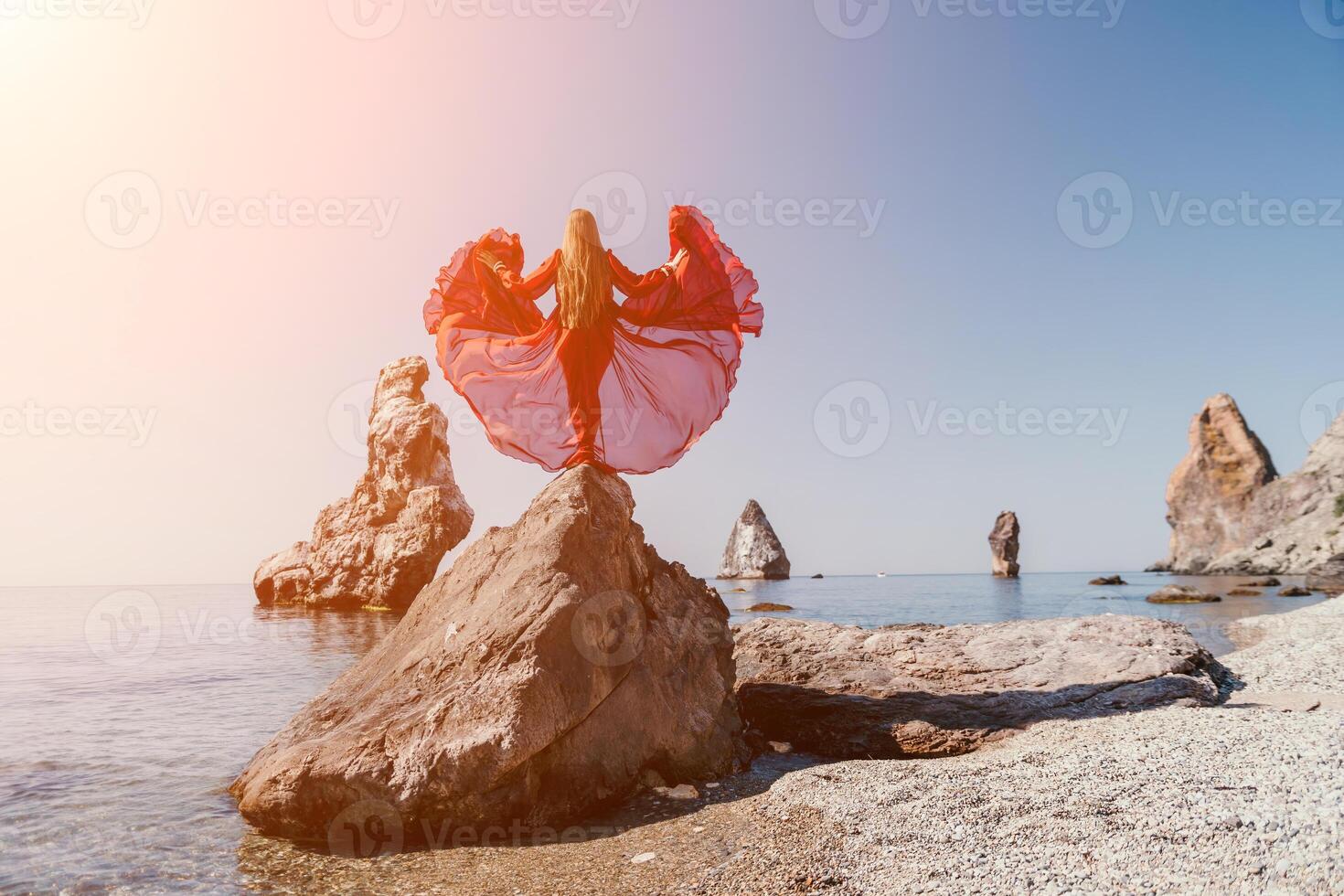 Woman travel sea. Young Happy woman in a long red dress posing on a beach near the sea on background of volcanic rocks, like in Iceland, sharing travel adventure journey photo