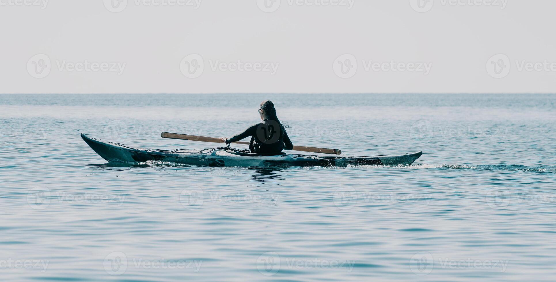 Woman sea kayak. Happy smiling woman in kayak on ocean, paddling with wooden oar. Calm sea water and horizon in background. Active lifestyle at sea. Summer vacation. photo
