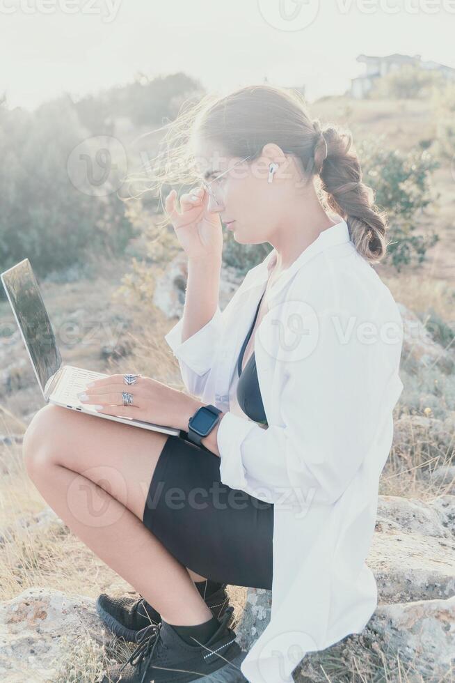Woman park laptop. Young woman in glasses, freelancer with laptop working in summer park on sunset. Happy smiling girl relieves stress from work. Freelance, remote work, digital nomad, travel concept photo
