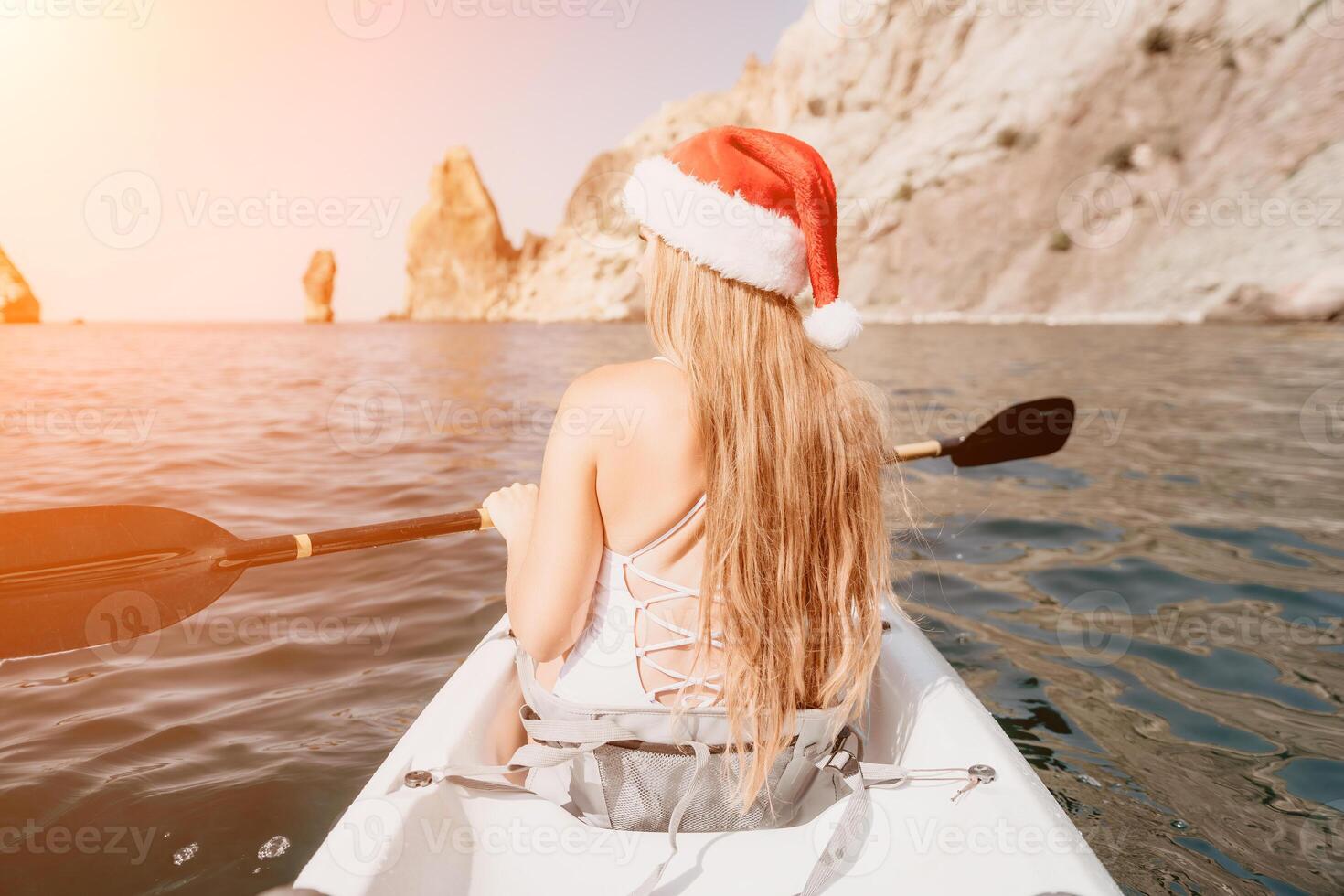 Woman in kayak back view. Happy young woman in Santa hat floating in kayak on calm sea. Summer holiday vacation and cheerful female people relaxing having fun on the boat. photo